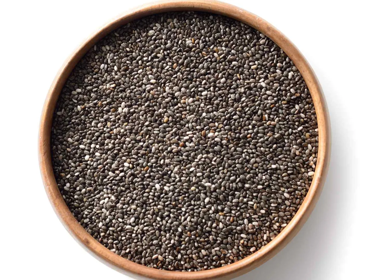 A copper bowl filled with chia seeds on a white background