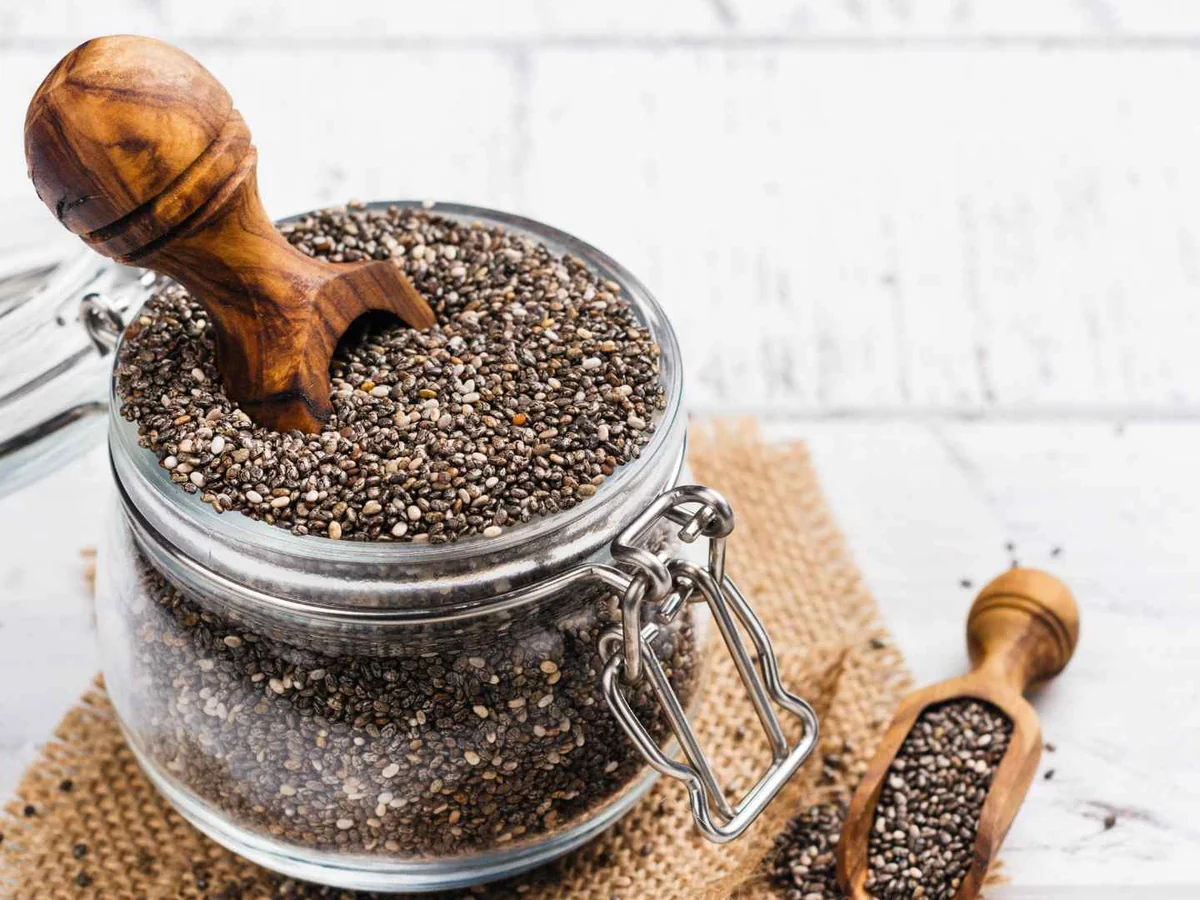 A glass jar and wooden scoop filled with chia seeds