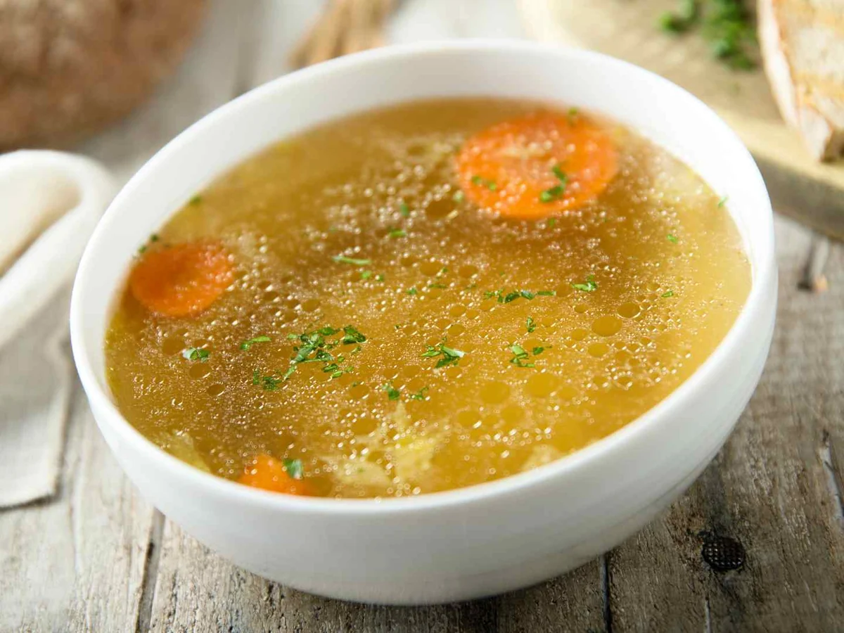 A bowl of chicken broth with carrot pieces