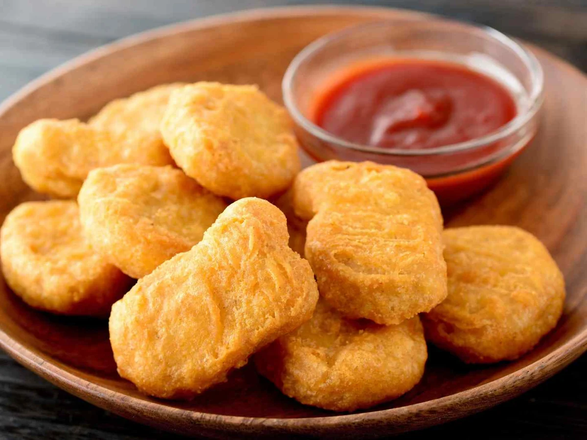 Breaded chicken nuggets on a wooden plate with ketchup