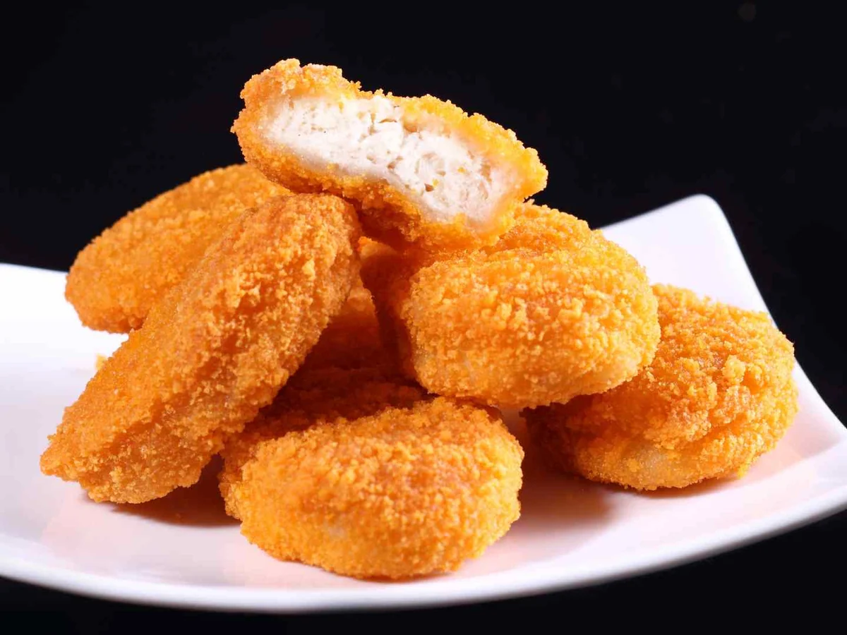 Breaded chicken nuggets stacked on a white plate against black