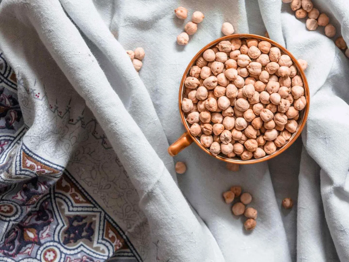 Dry chickpeas in a copper measuring cup on patterned cloth.