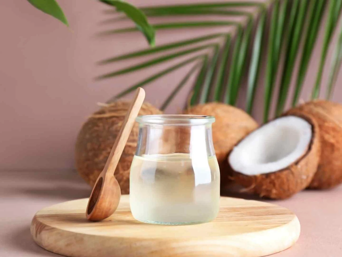 A small glass of clear coconut water beside whole and halved coconuts.
