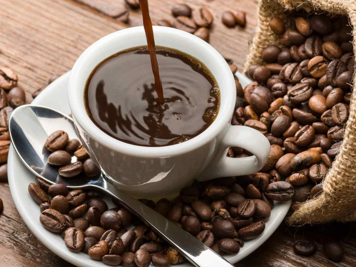 A cup of dark coffee surrounded by roasted coffee beans.