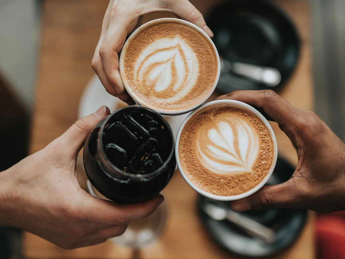 Three people holding one black coffee and two lattes viewed from above.