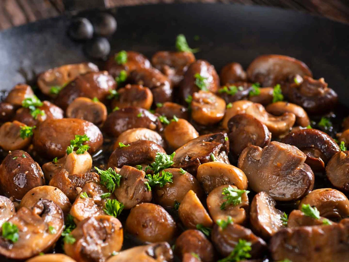 Glossy cooked mushrooms in a black pan with chopped parsley.