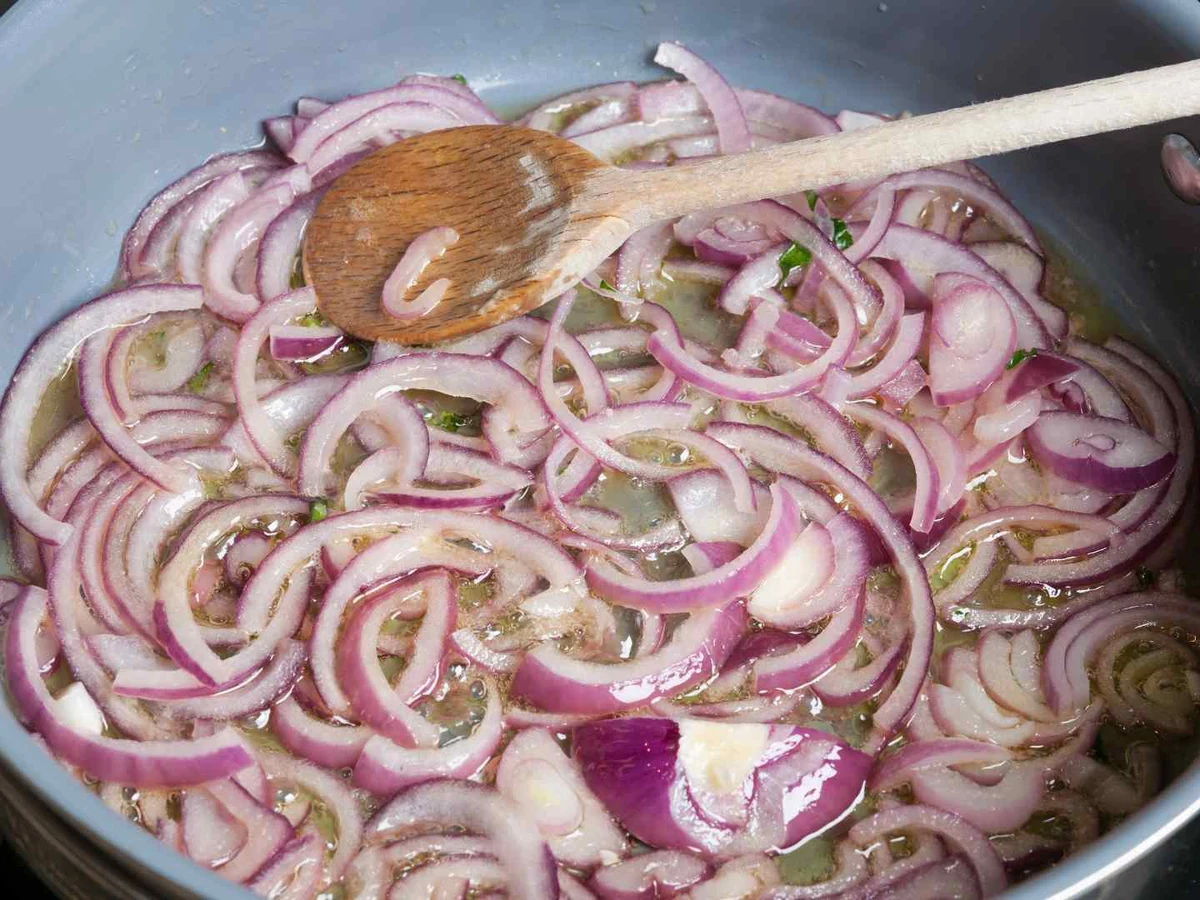 Thin red onion rings cooking in liquid in a black pan.