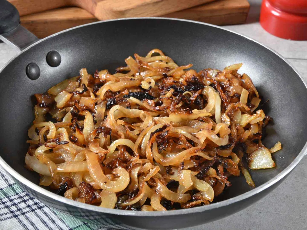 Browned sliced onions in a black frying pan on a kitchen counter.