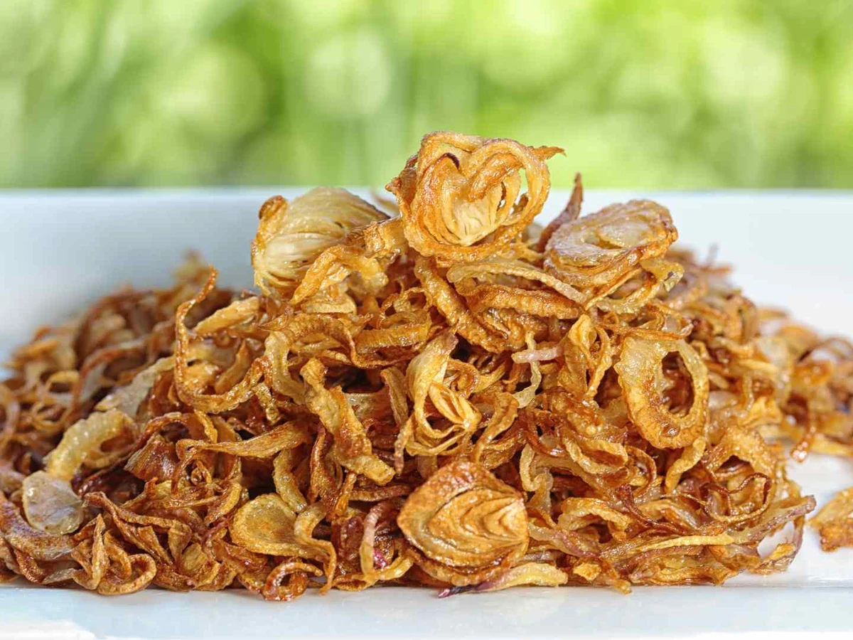 A mound of crisp fried onion strands on a white plate.