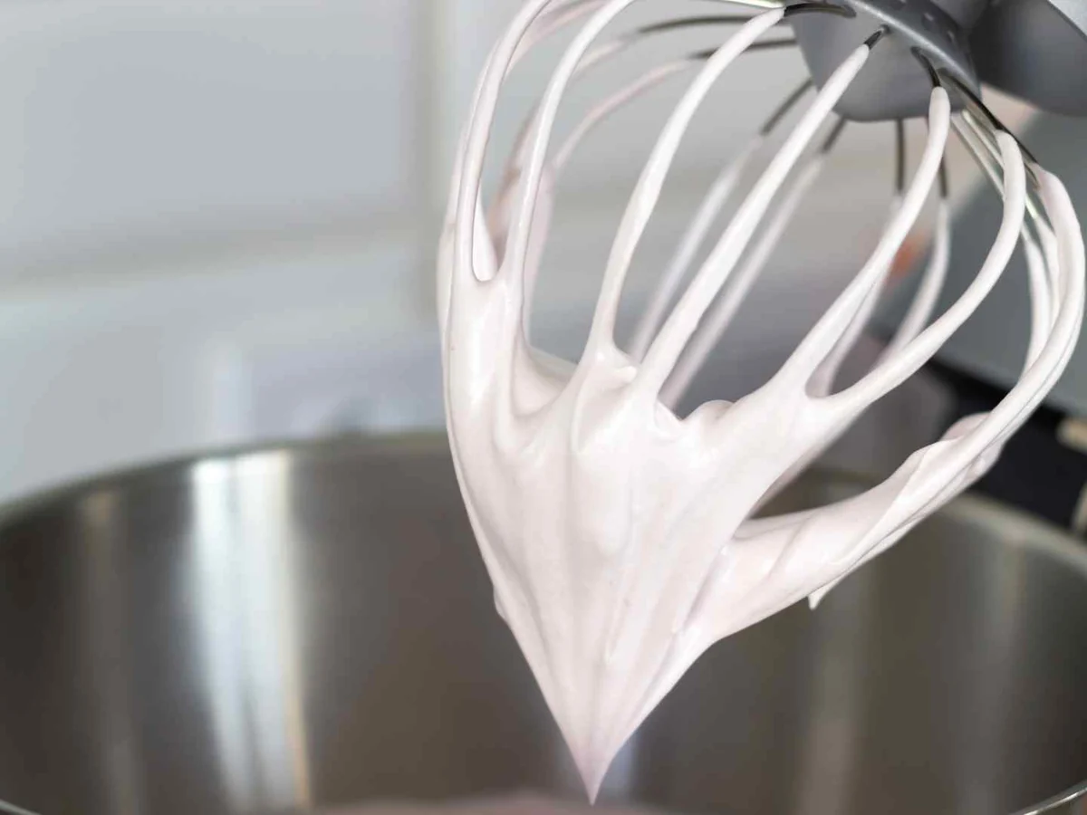 White whipped topping clinging to a mixer whisk above a metal bowl