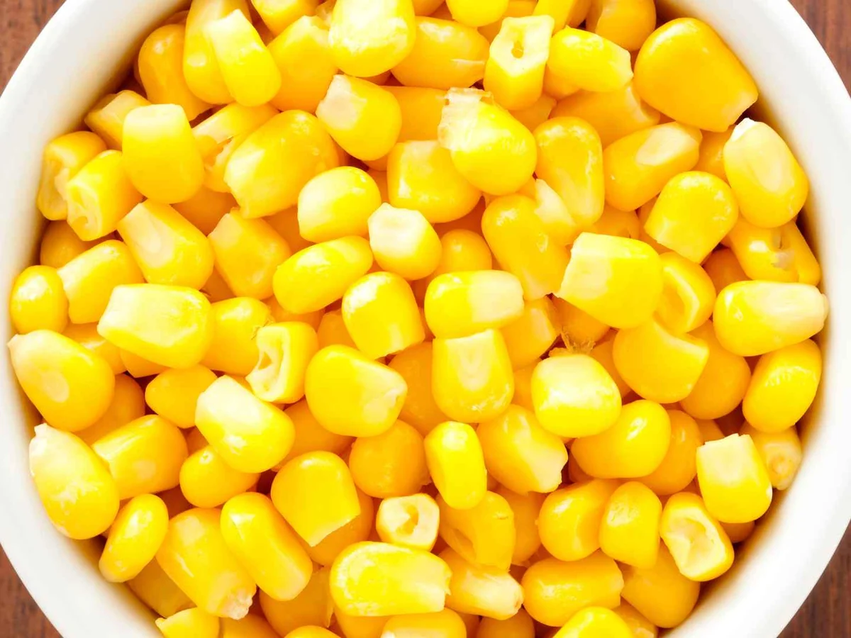 A white bowl filled with bright yellow cooked corn kernels