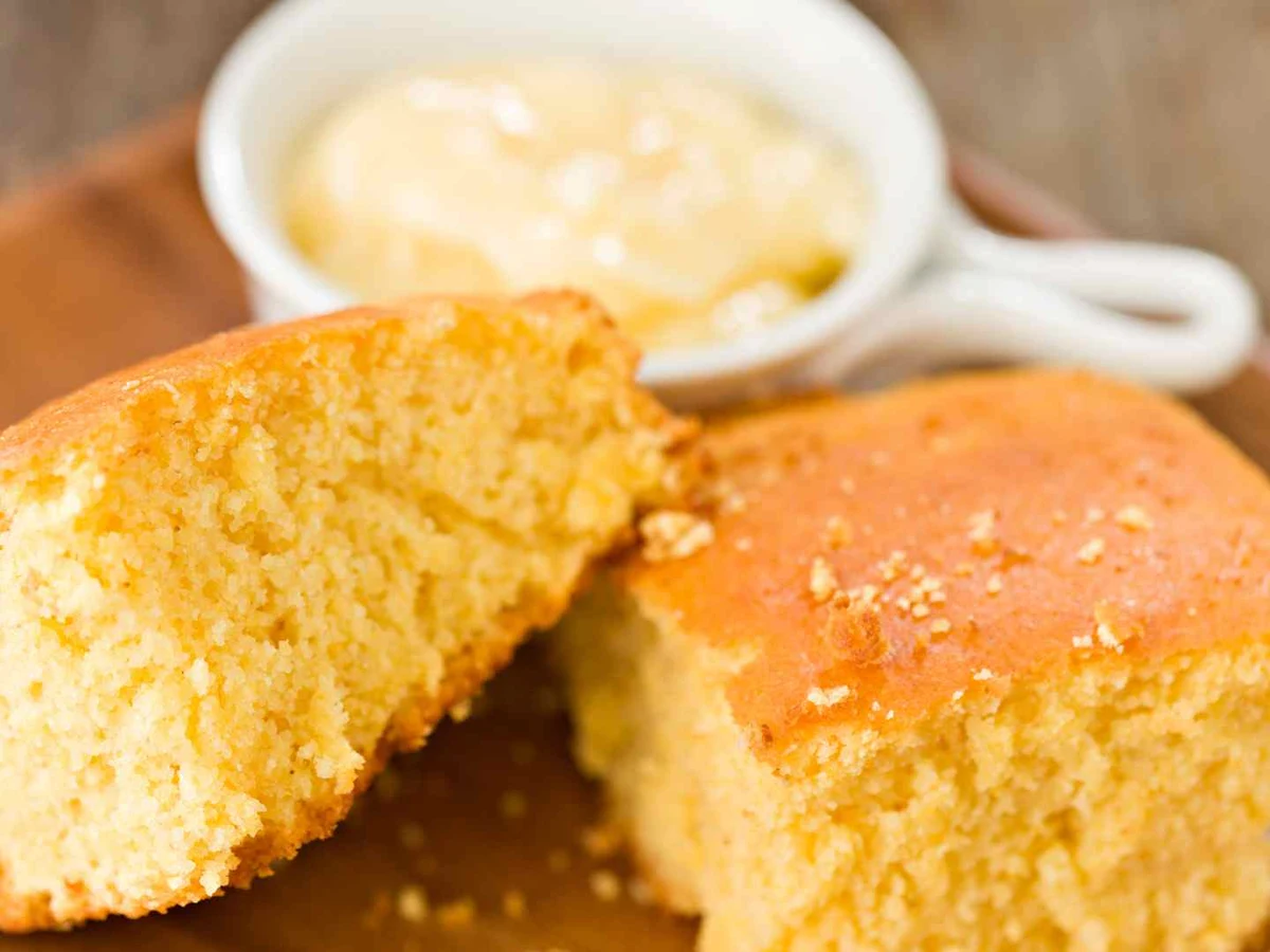 Cornbread wedges on a wooden board with a small bowl of butter.