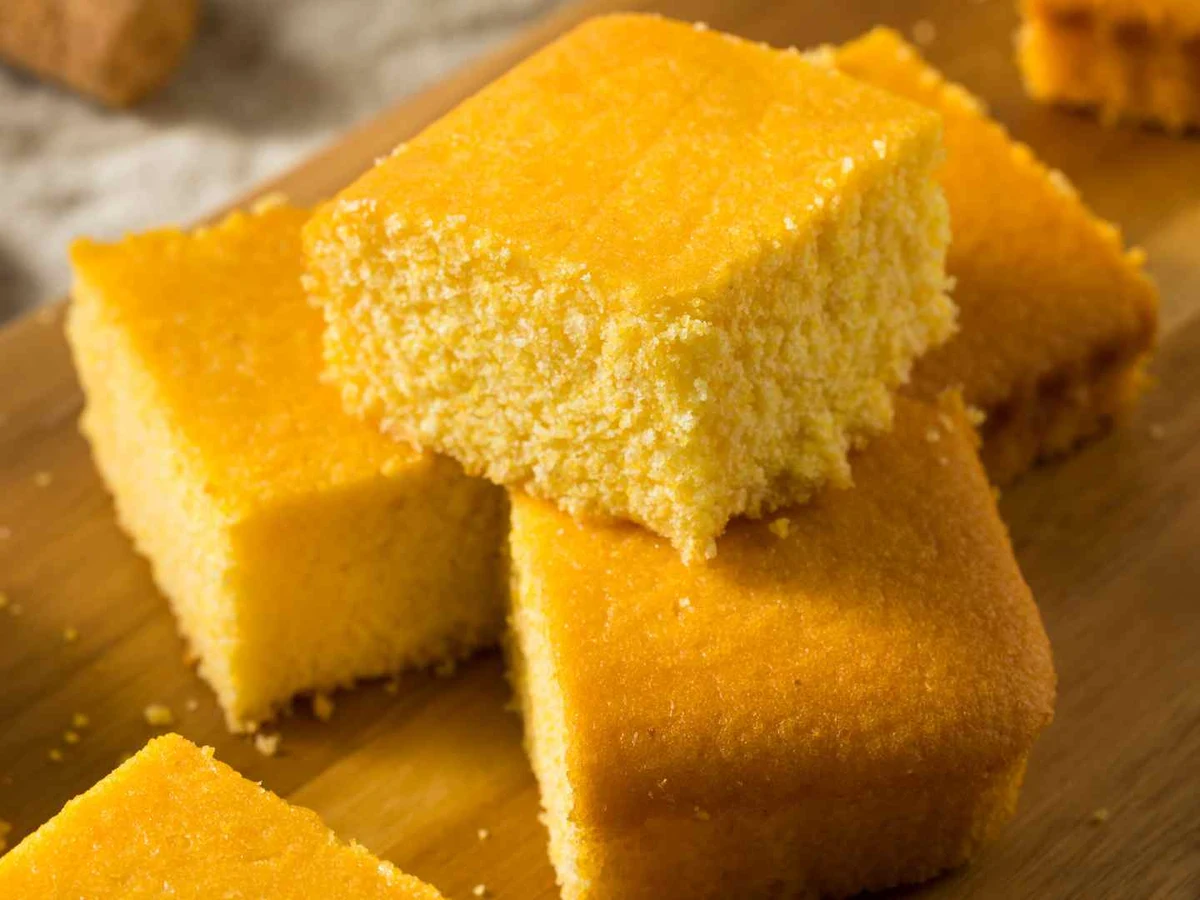 Thick square pieces of golden cornbread stacked on a wooden board.