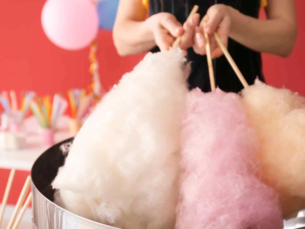 White, pink, and tan cotton candy cones being held above a machine.