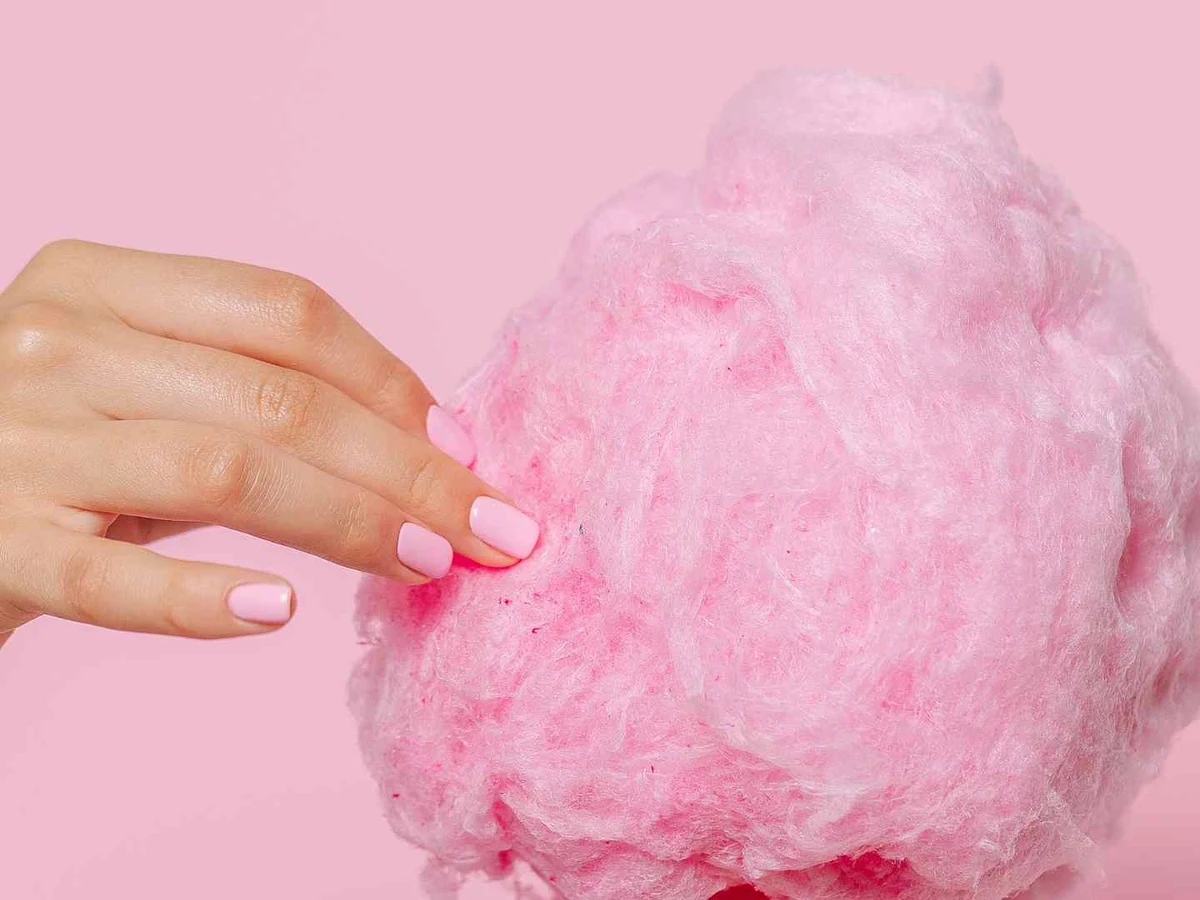 A hand pinching a large tuft of pink cotton candy against pink.