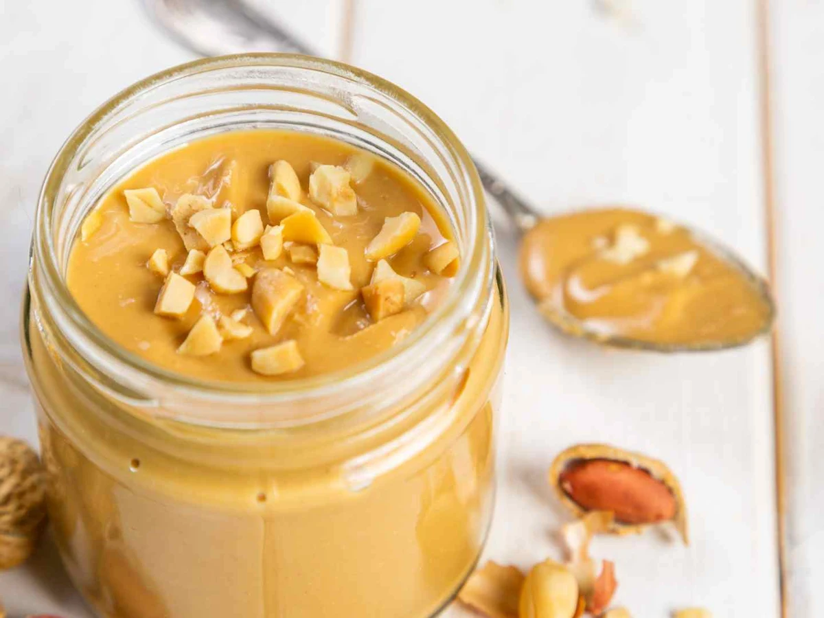 Chunky peanut butter in a glass jar topped with chopped peanuts.