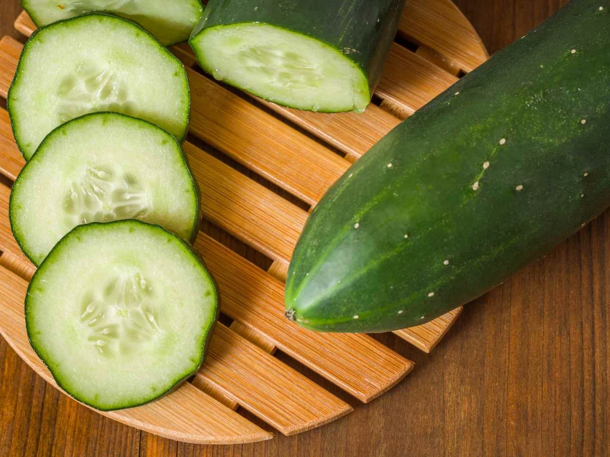 A whole cucumber and several round cucumber slices on a wooden board