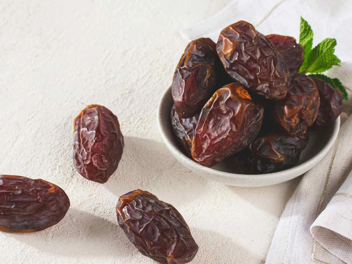 Brown dates in a ceramic bowl on a white cloth