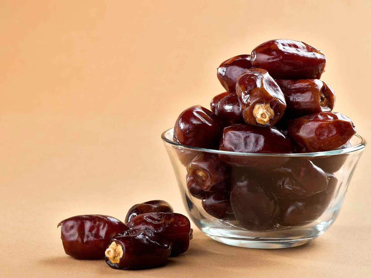 Brown dates piled in a glass bowl on a peach background