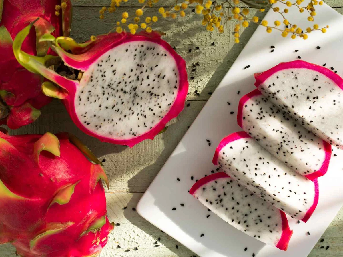 Sliced white dragon fruit on a white plate with whole fruit nearby