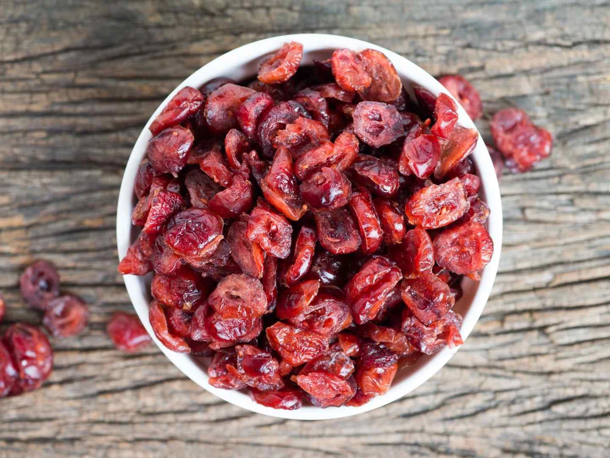 A white bowl of dried cranberries on a rustic wooden table