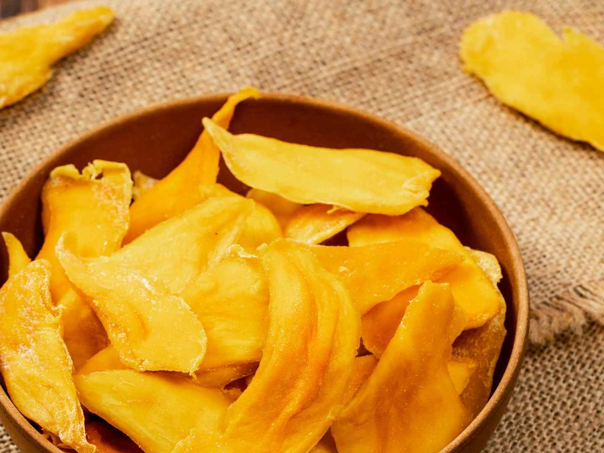 Dried mango slices filling a wooden bowl on burlap.