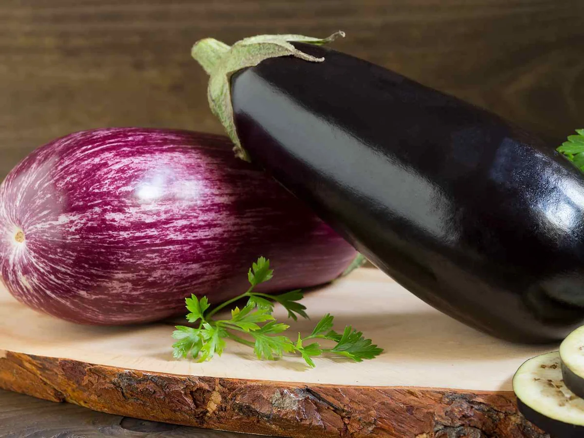 Purple eggplants, one sliced, on a wooden board