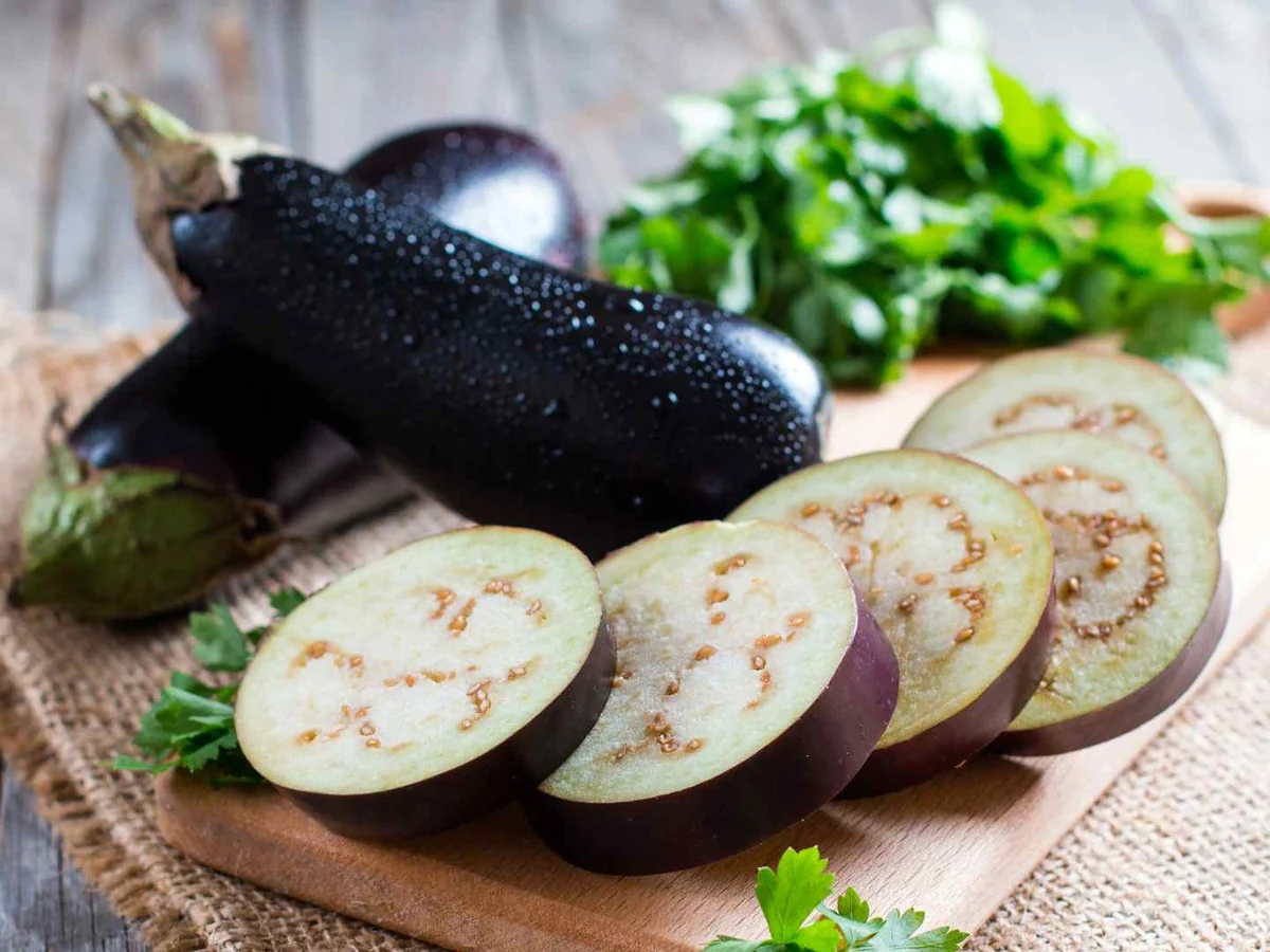 Two whole eggplants and several round slices on a cloth-covered table