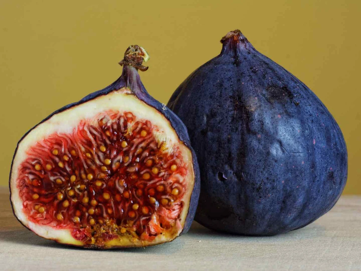 One whole fig and one halved fig with red seeded flesh on a mustard background.