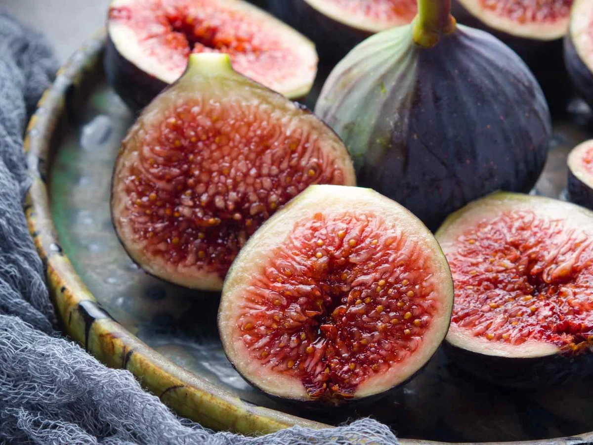 Fresh whole and halved figs arranged on a dark plate.