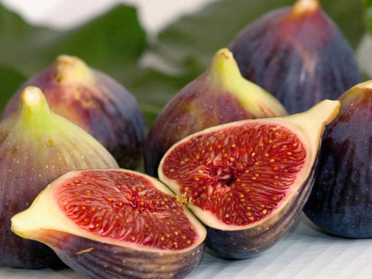 Fresh whole and halved purple figs arranged on a pale surface.