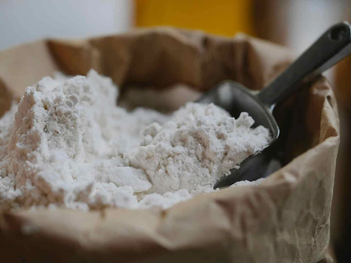 White flour in a paper-lined sack with a black scoop.