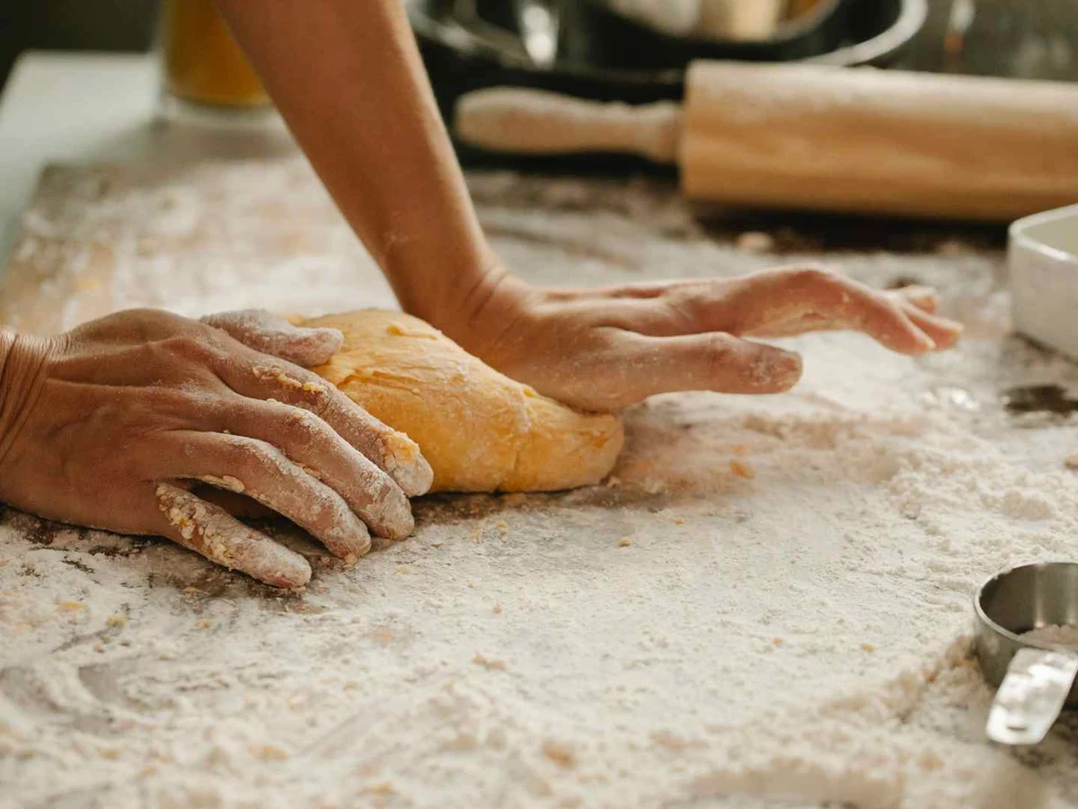 Flour-covered hands kneading dough on a heavily floured work surface.