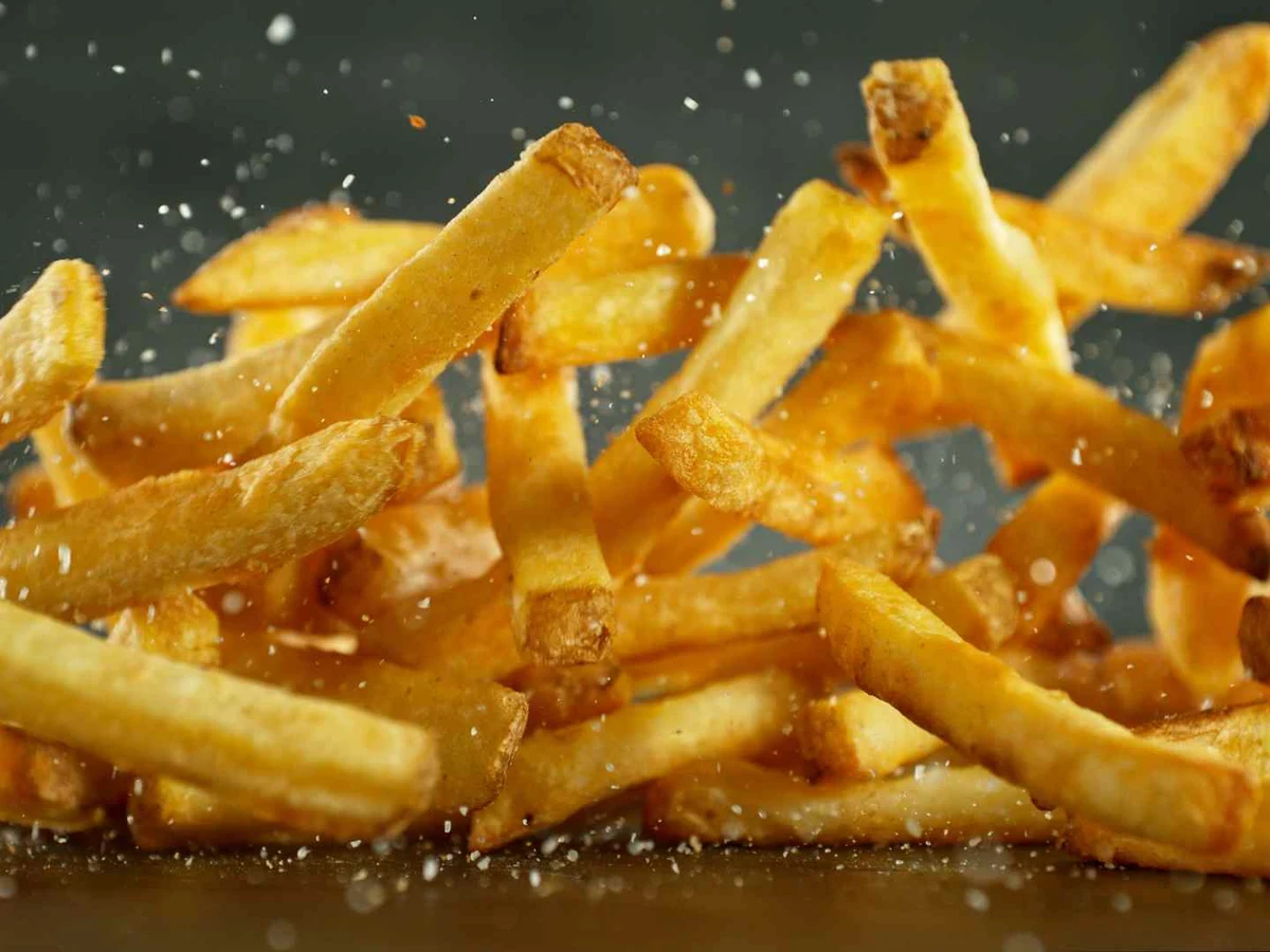 French fries falling through the air with salt crystals against a dark background.