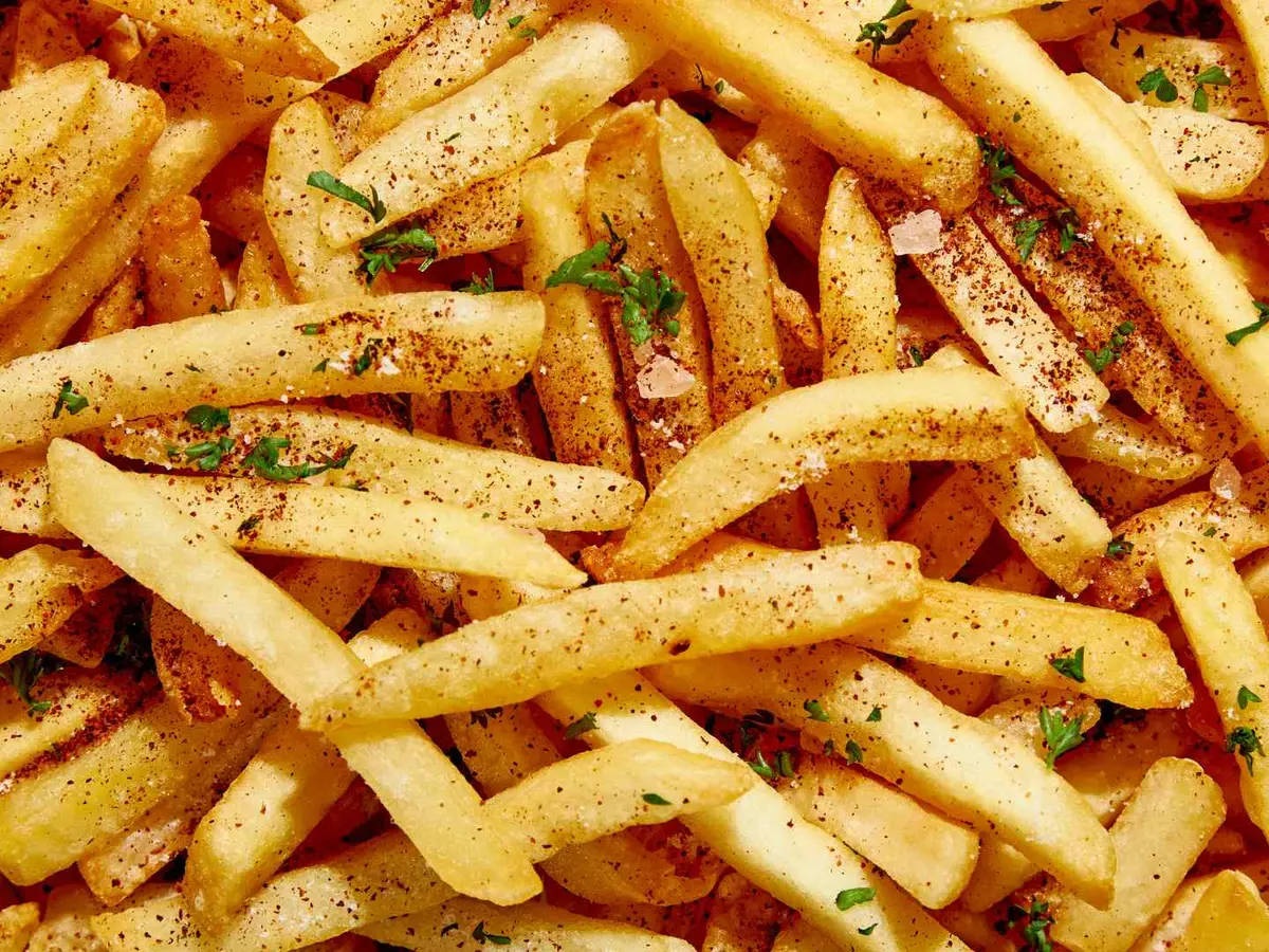 French fries dusted with red seasoning and green herbs fill the frame.