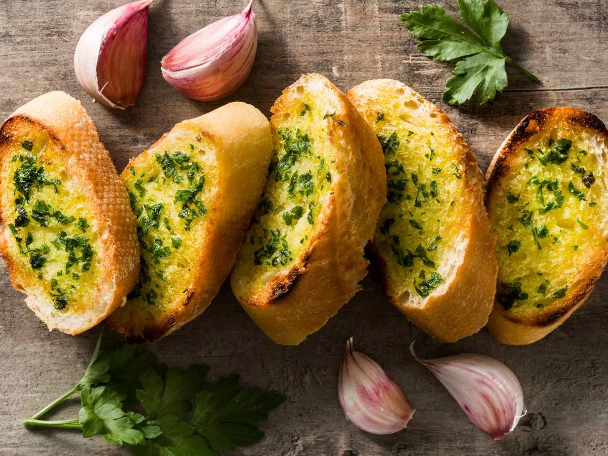 Slices of garlic bread with herbs beside garlic cloves