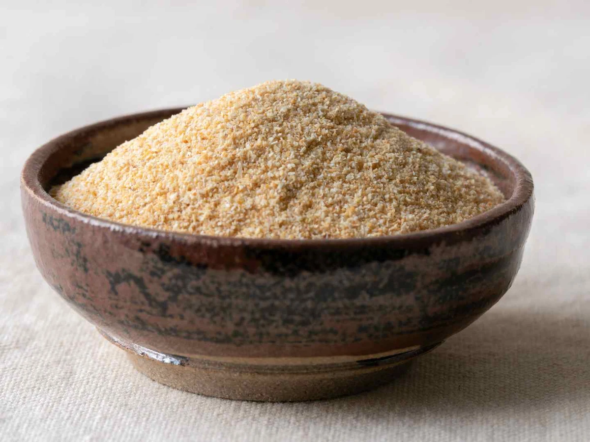 A bowl of tan garlic powder surrounded by whole garlic cloves.