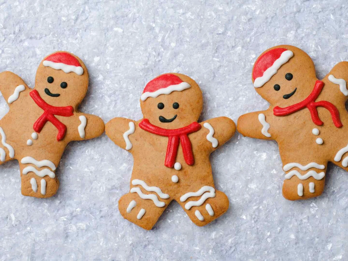 Three decorated gingerbread people lying on a snowy surface