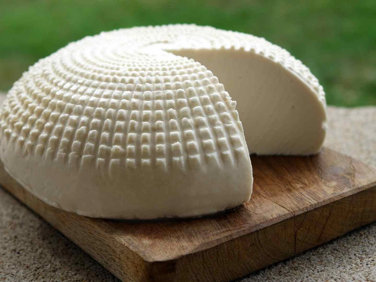 Two white rounds of fresh goat cheese on a wooden board outdoors.