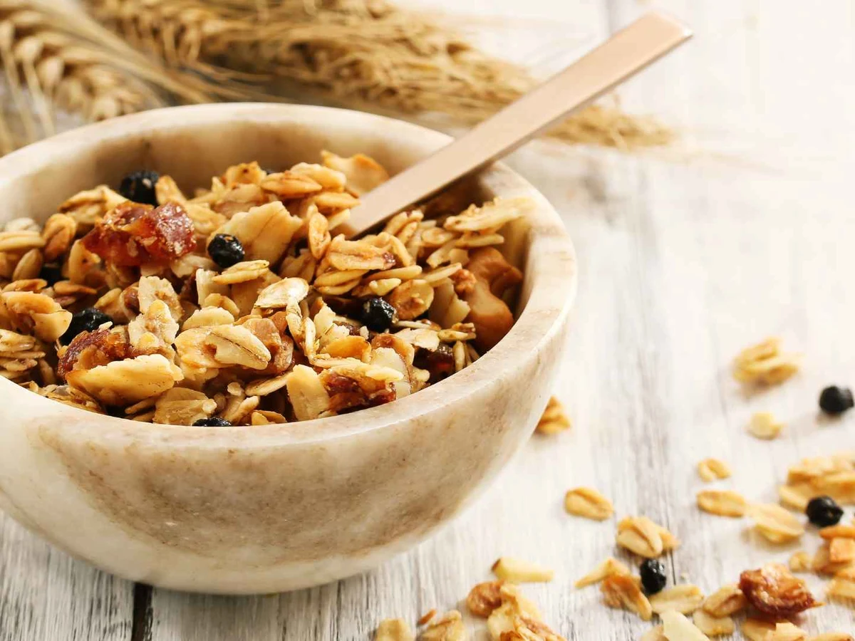 A bowl of granola with nuts and dried fruit on a pale table.