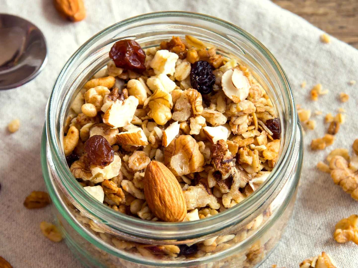 Granola containing oats, almonds, walnuts, and dried fruit in a glass jar.