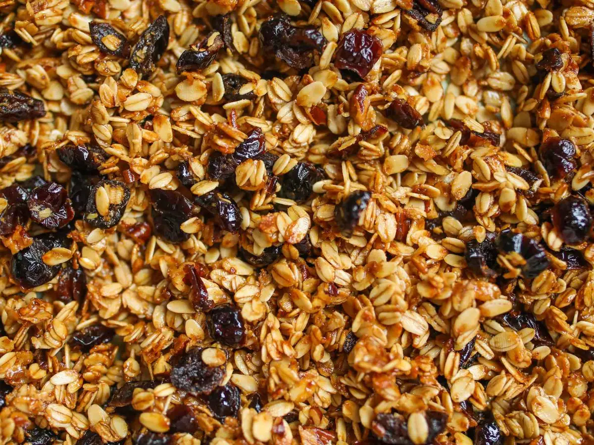 A close-up layer of toasted granola with oats, seeds, and dark dried fruit.