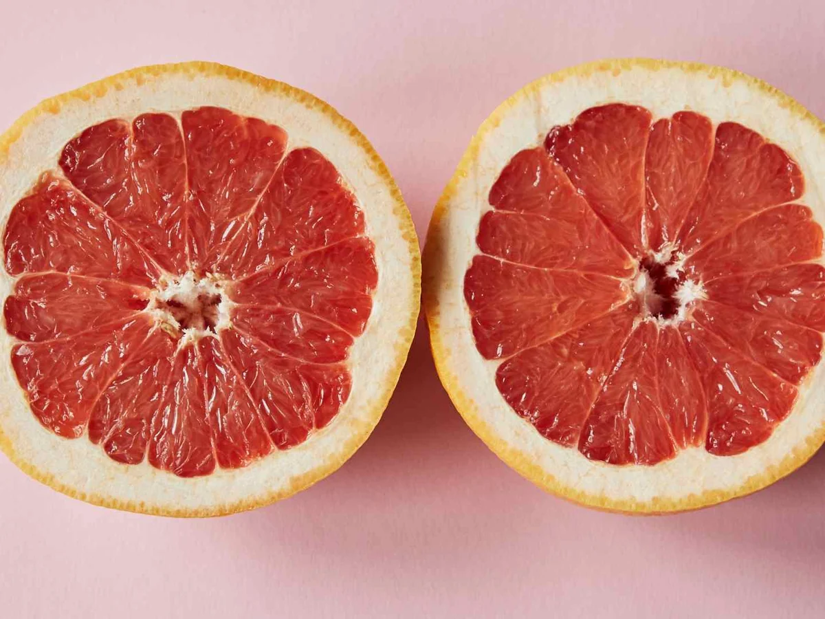 Two halved pink grapefruit on a pink background