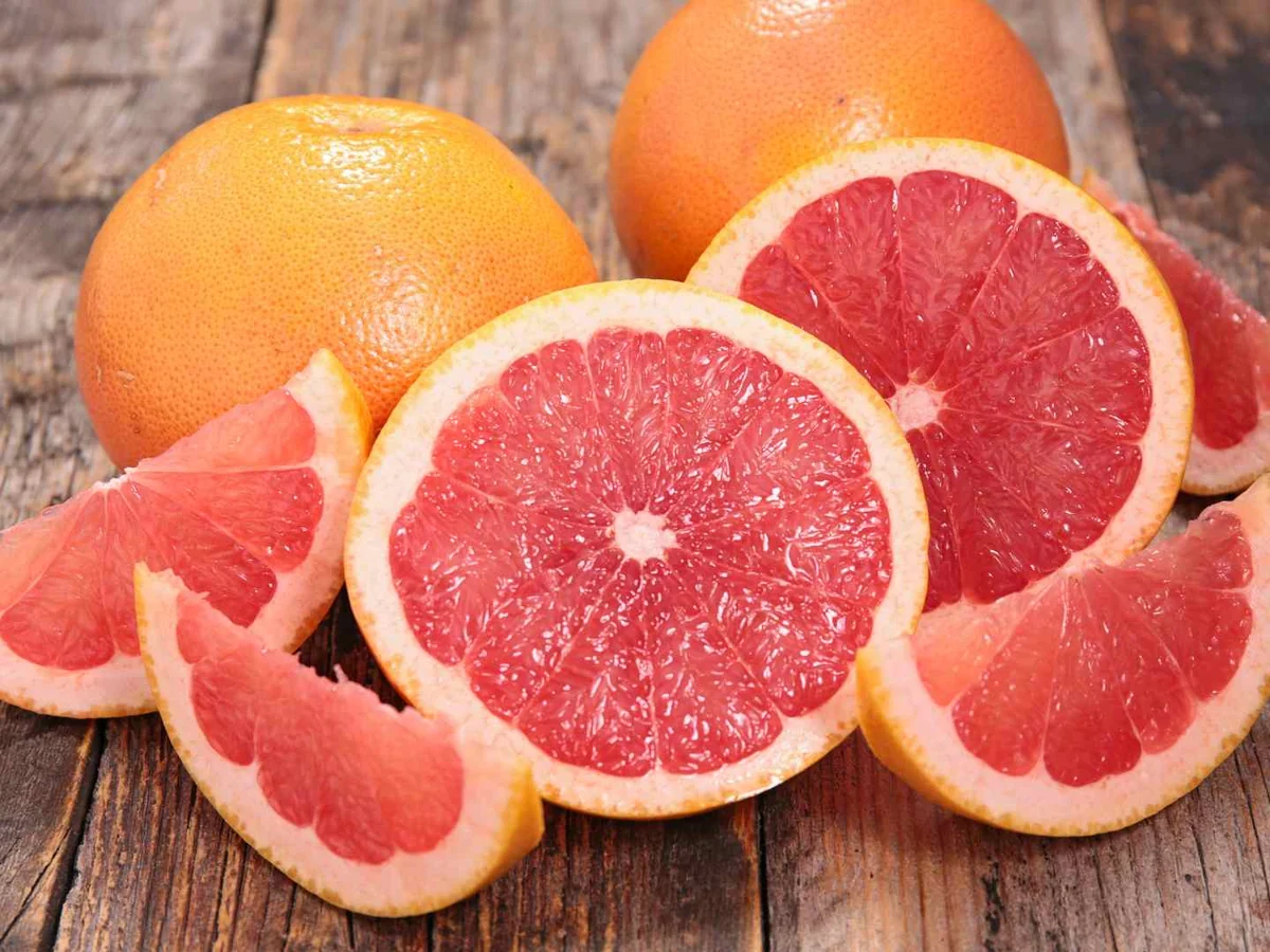 Whole and sliced pink grapefruit on a wooden table