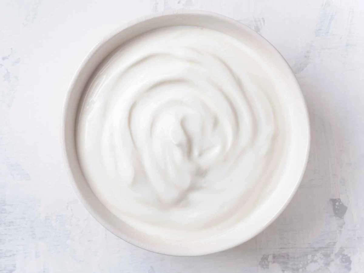 Overhead view of smooth white yogurt swirled in a white bowl on a pale surface.