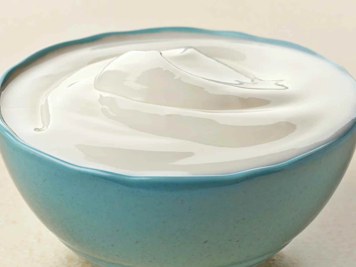 Smooth white yogurt fills a turquoise ceramic bowl against a light background.