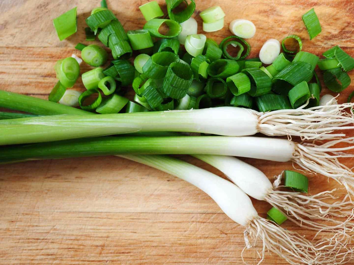 Whole and chopped green onions on a cutting board