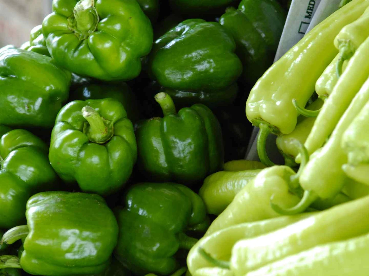 Green bell peppers and long pale green peppers packed together at a market.