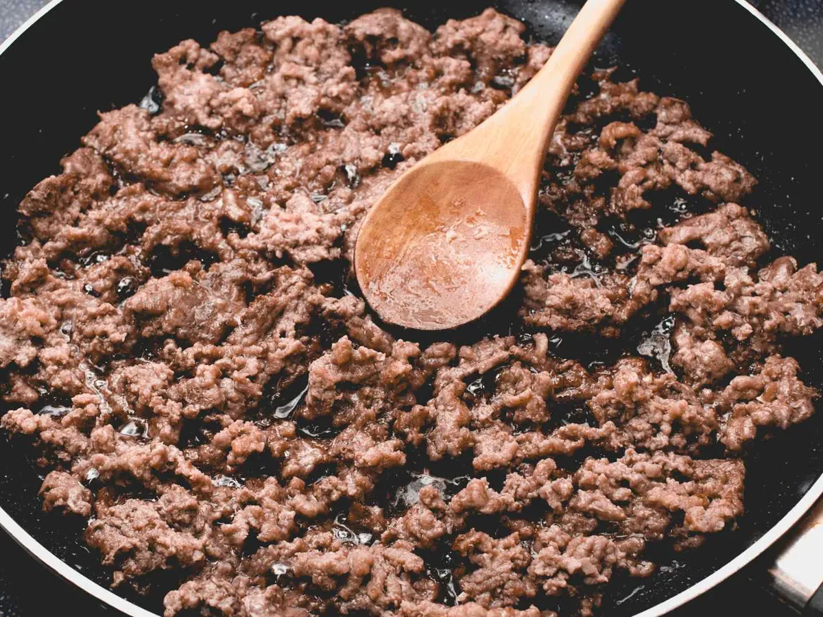 Ground beef cooking in a frying pan with a wooden spoon