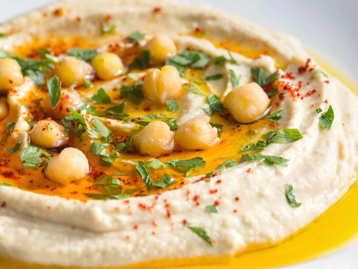 A plate of hummus topped with chickpeas, herbs, oil, and paprika